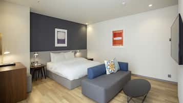 A modern hotel room with a large bed, a sofa, a small table, and a flat-screen TV mounted on the wall.