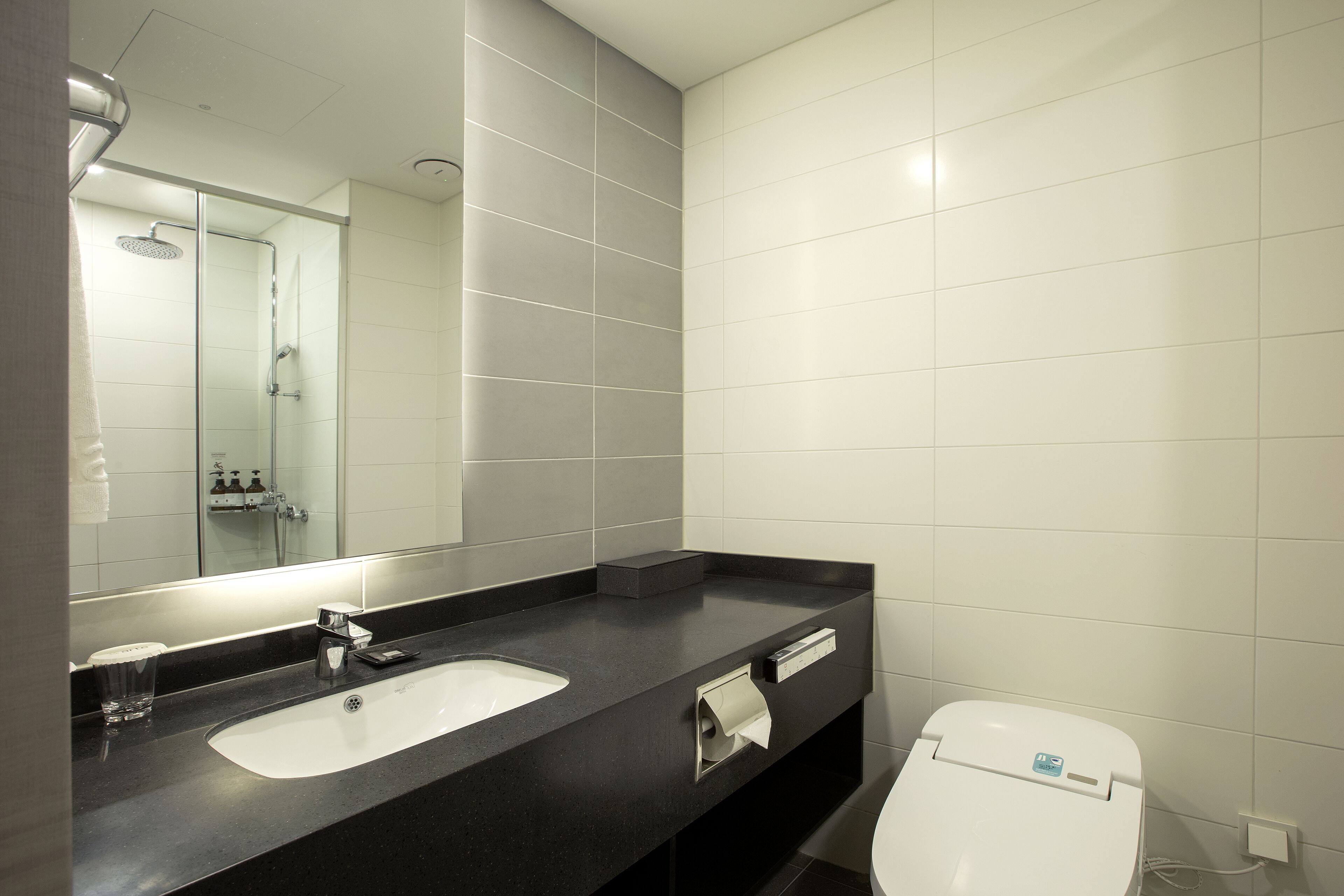 A modern bathroom with a black countertop, a white sink, a mirror, and a toilet.