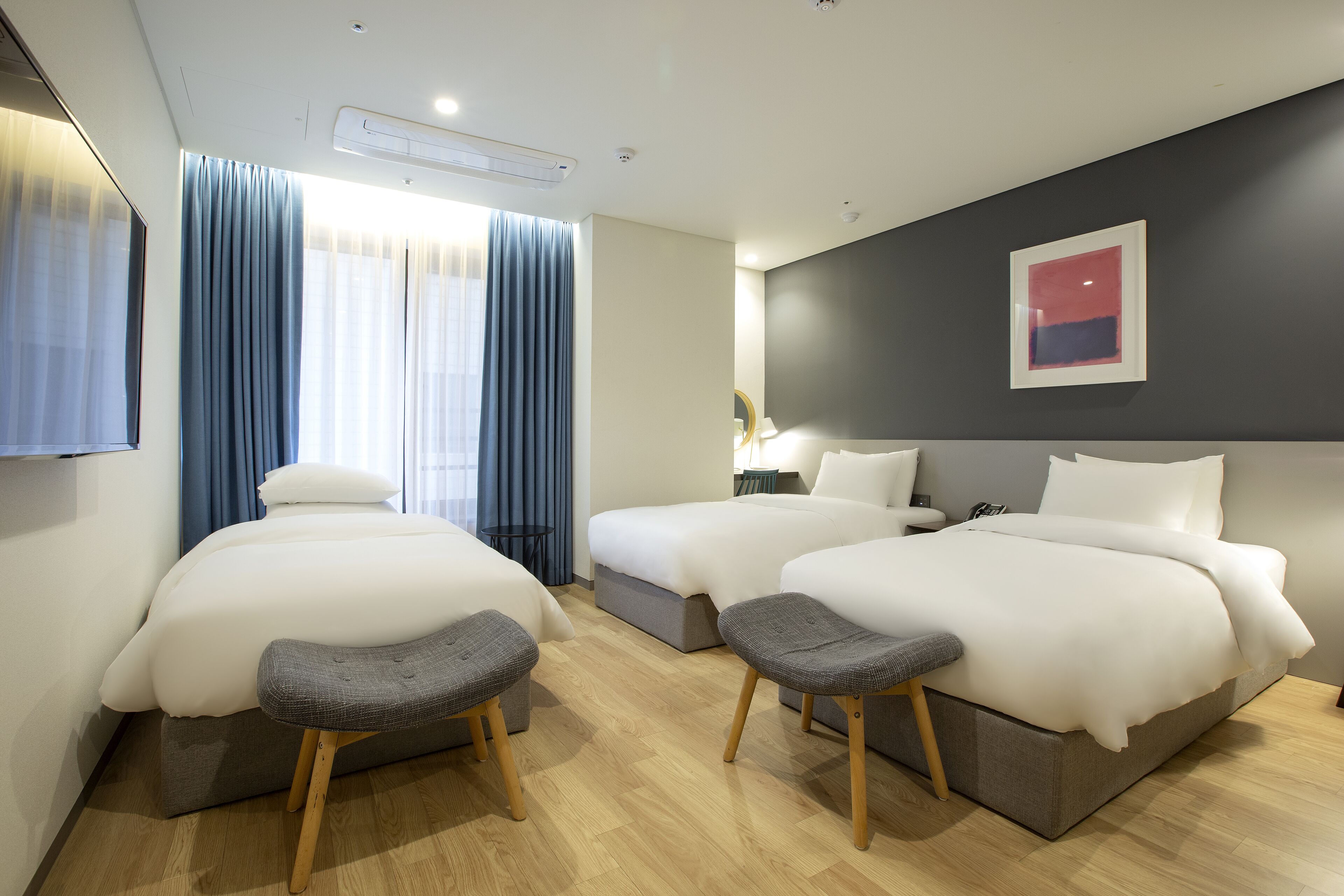 A hotel room with two beds, a small table, and a bench.