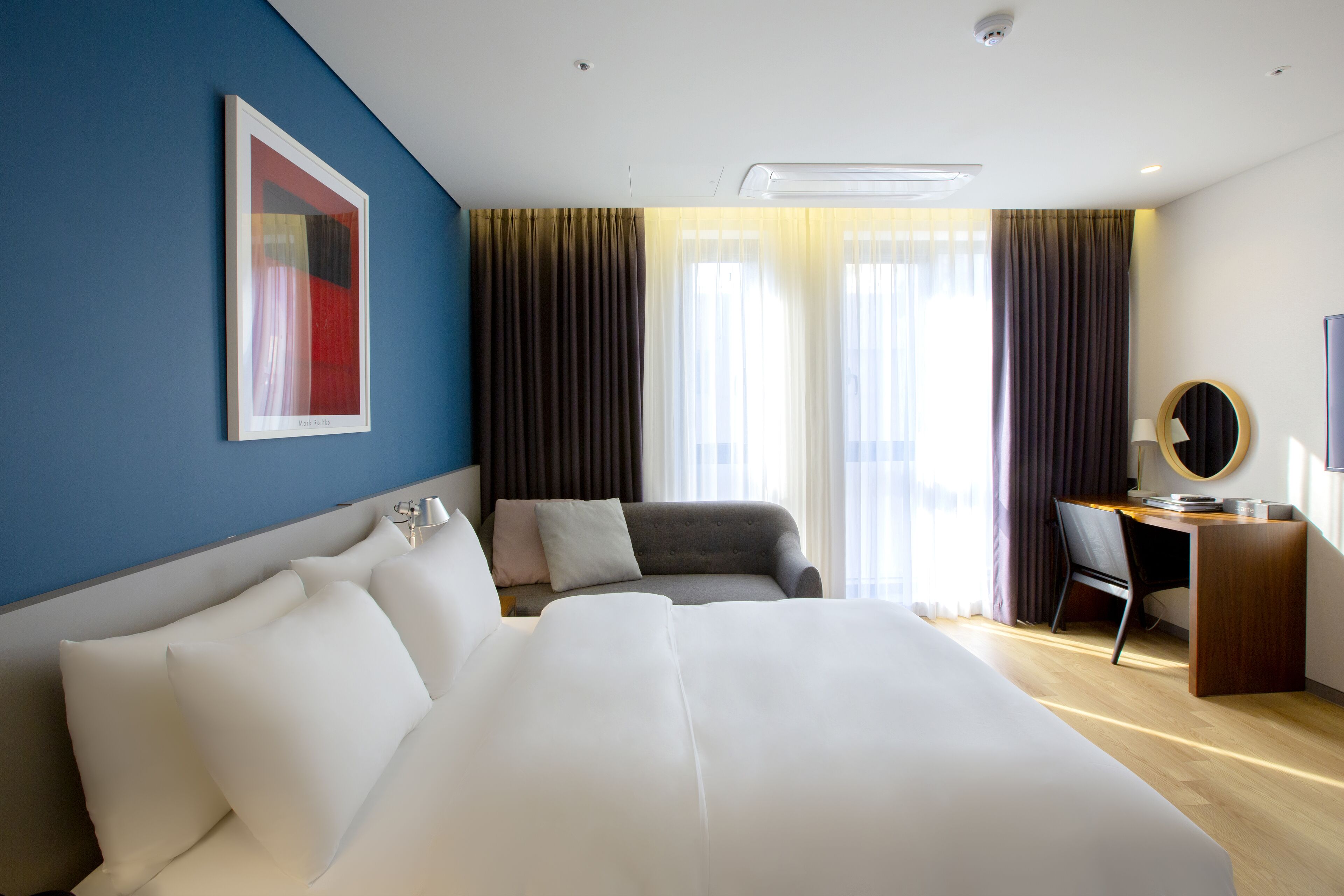 A modern hotel room with a large bed, a desk, and a chair.
