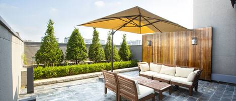 A patio with a wooden bench, a sofa, and a table under a large umbrella.