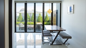 A modern dining area with a large table and benches, large windows with a view of greenery and buildings, and a hanging light fixture. - Hotel Arte (Suwon)