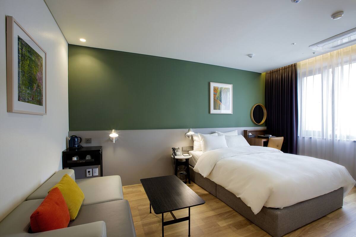 Una habitación de hotel con cama, sofá, una pequeña mesa, escritorio y lámpara.