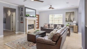 A modern living room with a sectional sofa, a coffee table, and a fireplace. There is a large mirror above the fireplace and a ceiling fan. - Walkable South Congress Home + Guest House (Austin)