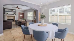 A dining area with a round table, blue chairs, and a white tablecloth. There is a fireplace with a mantel and a ceiling fan above it. - Walkable South Congress Home + Guest House (Austin)