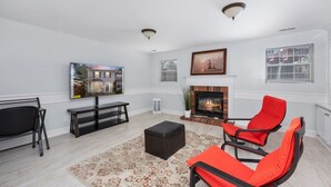 Una sala de estar moderna con chimenea, un televisor montado en la pared y un amplio ventanal con persianas.