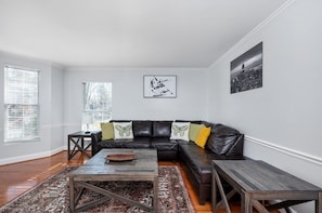 Een woonkamer met een zwarte leren bank, een houten salontafel en een vloerkleed met dessin.