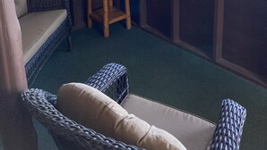 A cozy corner with wicker furniture, a small wooden stool, and large windows offering a view of trees and a body of water. - Cabin #1 - "Chickagami" (Carp Lake)