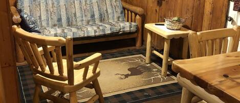 L’intérieur d’un chalet en bois, avec un canapé, deux fauteuils, une petite table et un téléviseur fixé au mur.