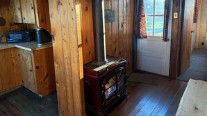 A wooden cabin interior with a wood stove, a microwave, and a door with curtains. - Cabin #1 - "Chickagami" (Carp Lake)