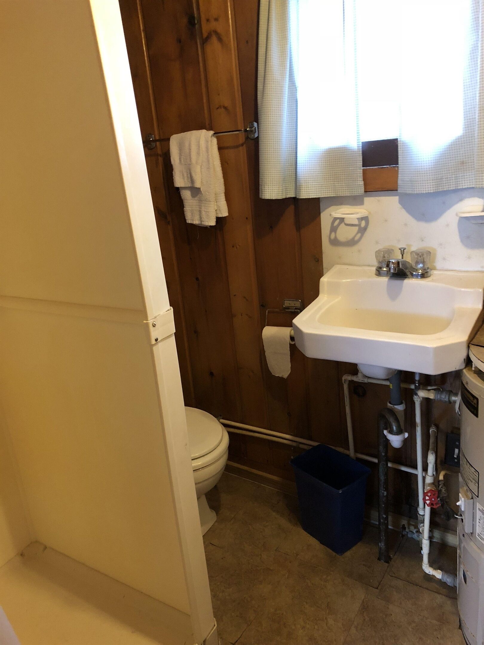 Un baño con puerta de madera, un lavamanos blanco, un inodoro y un cubo de basura azul.