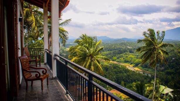 Un balcón con vistas a un paisaje exuberante, con palmeras y montañas a la distancia.