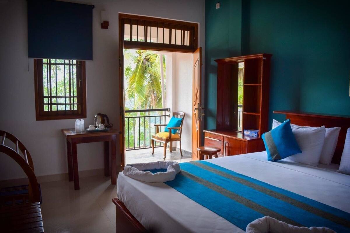 A hotel room with a bed, a desk, a chair, a small table, a wardrobe, and a balcony with a chair.