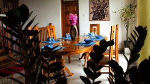 Un comedor con una mesa de madera dispuesta para cuatro personas, rodeada de sillas. Hay un jarrón con flores sobre la mesa, y un cuadro en la pared.