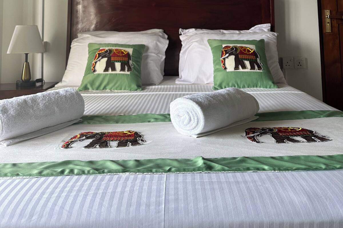 A neatly made bed with green and white pillows, a framed painting above, and a wooden headboard.