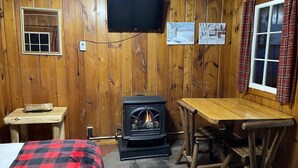 Ein gemütliches Cabin-Zimmer mit Holzofen, einem an der Wand montierten Fernseher und einem kleinen Tisch mit einer Bank.