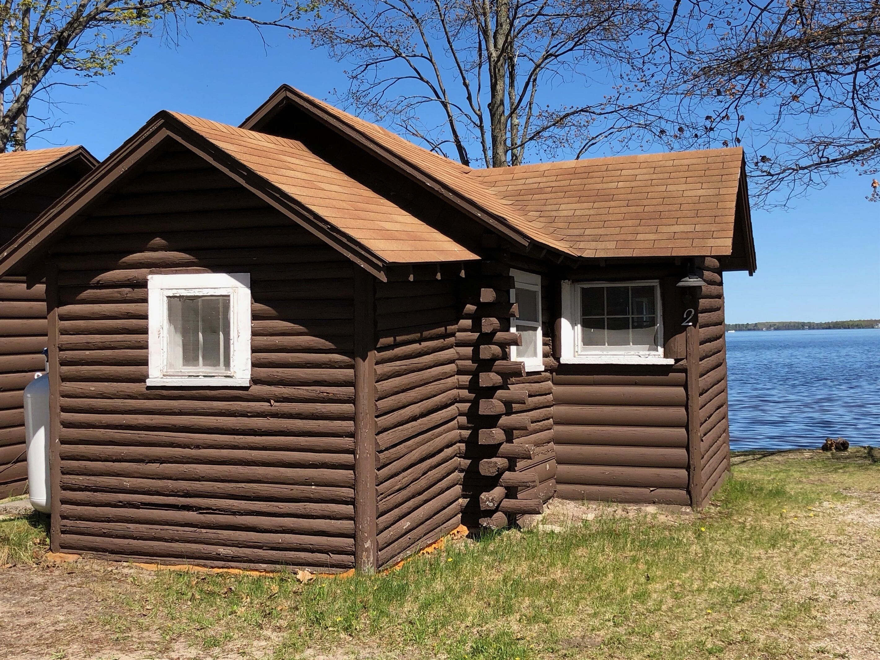 Due chalet in legno con tetti a falde, situati vicino a una superficie d'acqua, probabilmente un lago o un fiume.