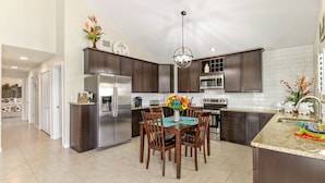 A modern kitchen with dark cabinetry, stainless steel appliances, a dining area with wooden chairs, and a central island with a vase of flowers.