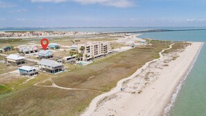 An aerial view of a coastal area with a beachfront hotel, a pier, and a road leading to the beach.