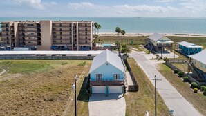 A coastal building complex with a large parking area and a view of the beach and ocean.