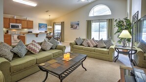 A spacious living area with a green sofa set, a coffee table, and a dining area in the background. - Luxury 4 Bedroom Florida Holiday Home with Pool & Spa (Davenport)