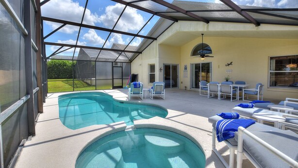 A covered outdoor swimming pool area with lounge chairs and a patio table. - Luxury 4 Bedroom Florida Holiday Home with Pool & Spa (Davenport)