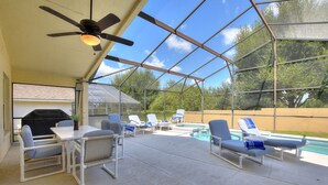 A covered outdoor area with a pool, lounge chairs, a table, and a ceiling fan. - Luxury 4 Bedroom Florida Holiday Home with Pool & Spa (Davenport)
