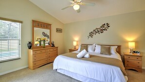 A bedroom with a bed, wooden dresser, nightstands, a ceiling fan, and a window with blinds. - Luxury 4 Bedroom Florida Holiday Home with Pool & Spa (Davenport)