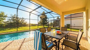 A covered outdoor area with a pool, a table with chairs, and a view of a grassy yard.
