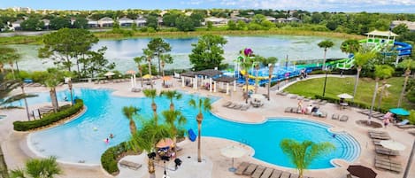 A resort pool area with a large central pool, a water slide, and lounge chairs.