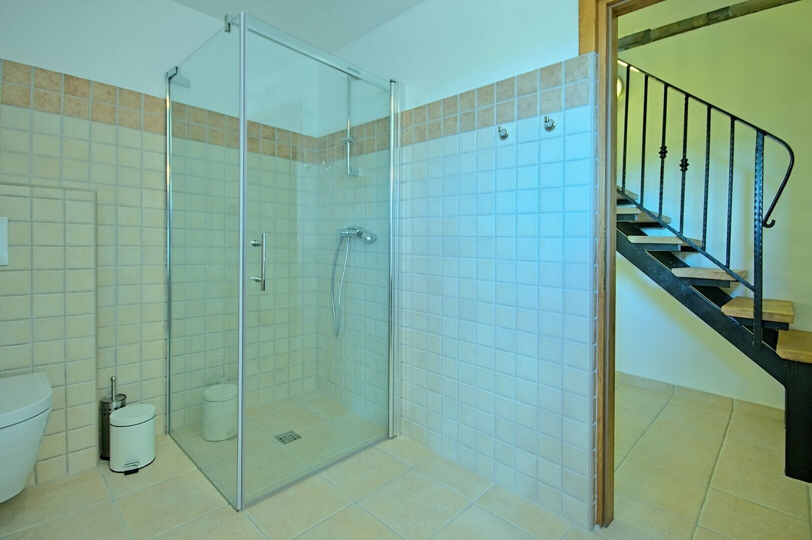 Een badkamer met een douche met glazen wand, toilet en prullenbak.