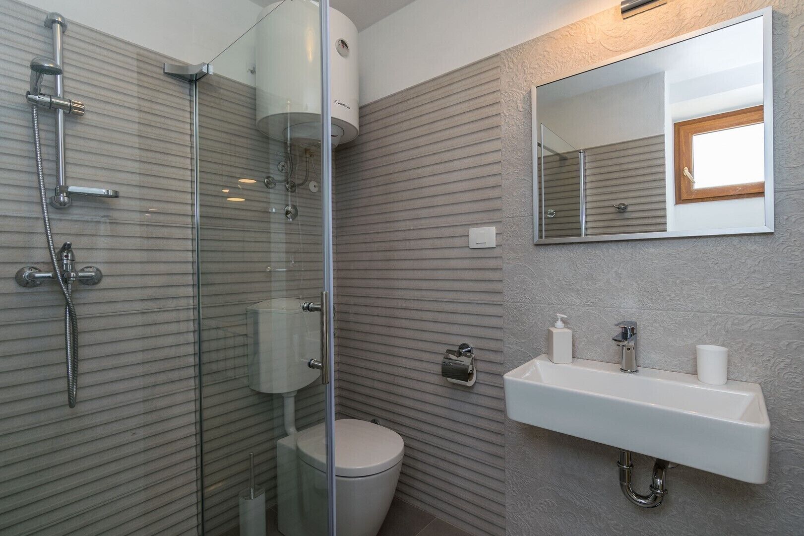 Un baño moderno con ducha envuelta en vidrio, inodoro y lavabo con espejo arriba.