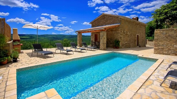 A swimming pool with lounge chairs, a stone building, and a view of green hills under a blue sky. - Villa Alba with breathtaking view from swiming pool, HEATED POOL, near Motovun (Livade)
