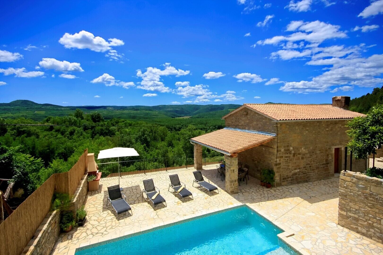A stone building with a tiled roof, a swimming pool, and outdoor seating.