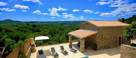 A stone building with a tiled roof, a swimming pool, and outdoor seating.