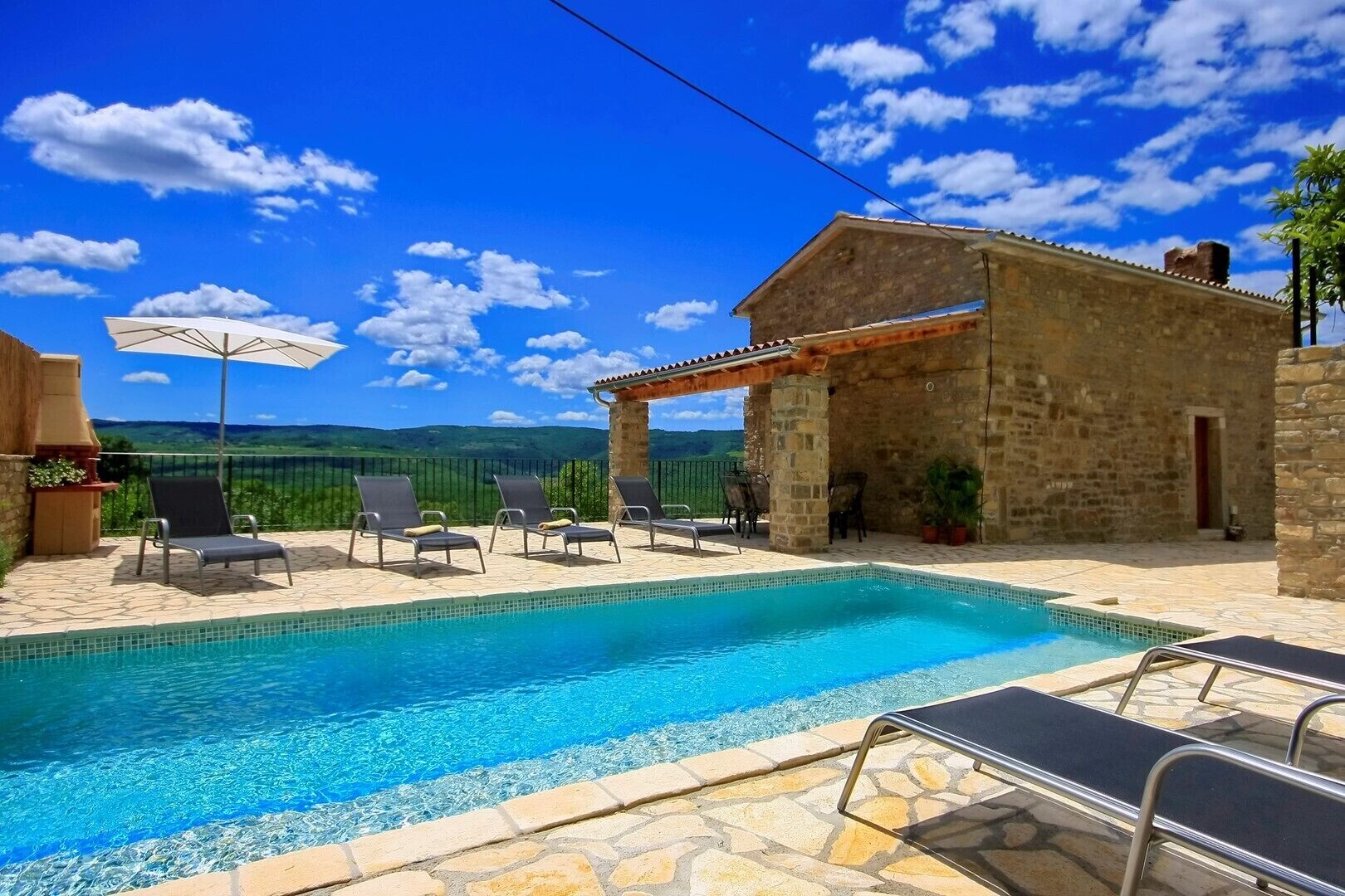 A swimming pool with lounge chairs and a stone building with a tiled roof.