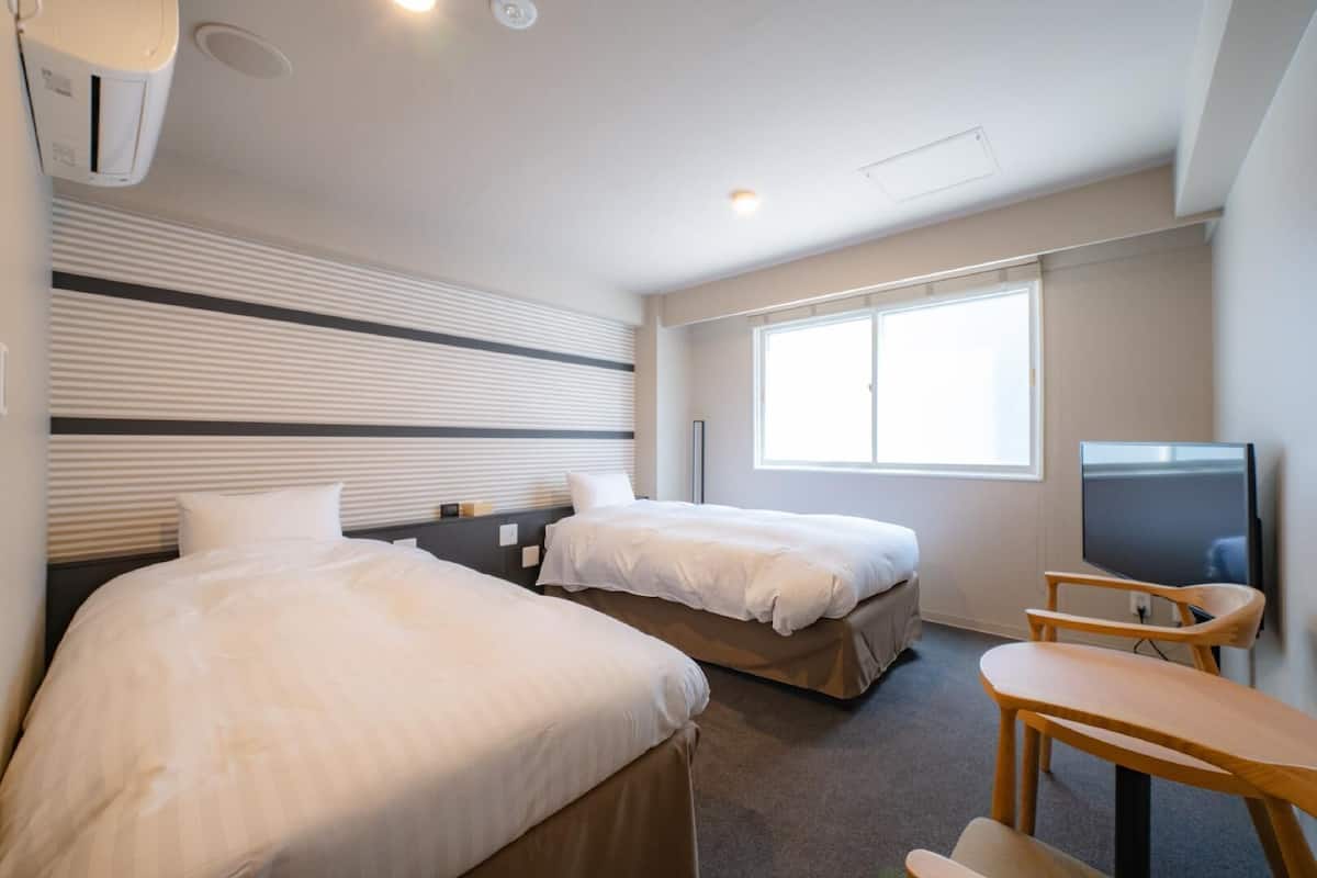 A hotel room with two beds, a TV, and a window.