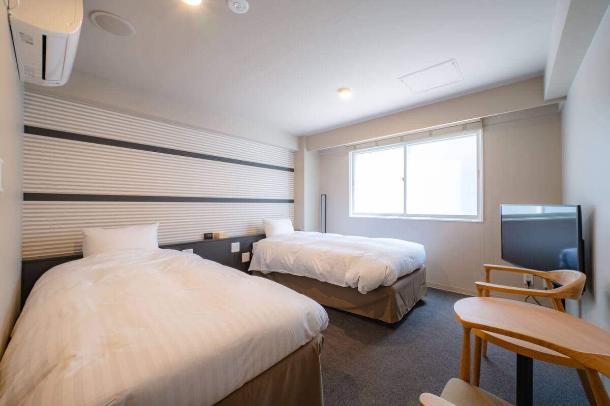 A hotel room with two beds, a TV, and a desk.