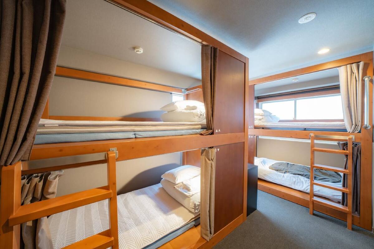 A bunk bed room with wooden frames, a window with curtains, and a ceiling light.