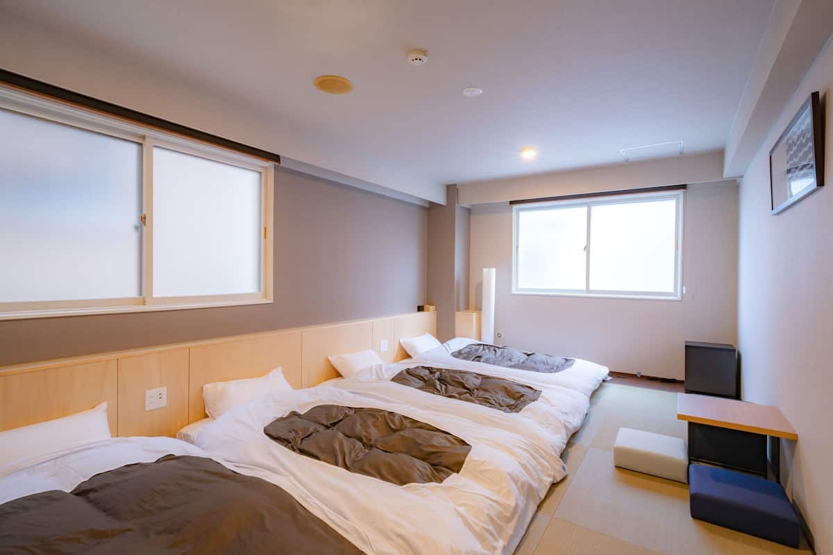 A modern hotel room with two beds, a small desk, and large windows providing natural light.