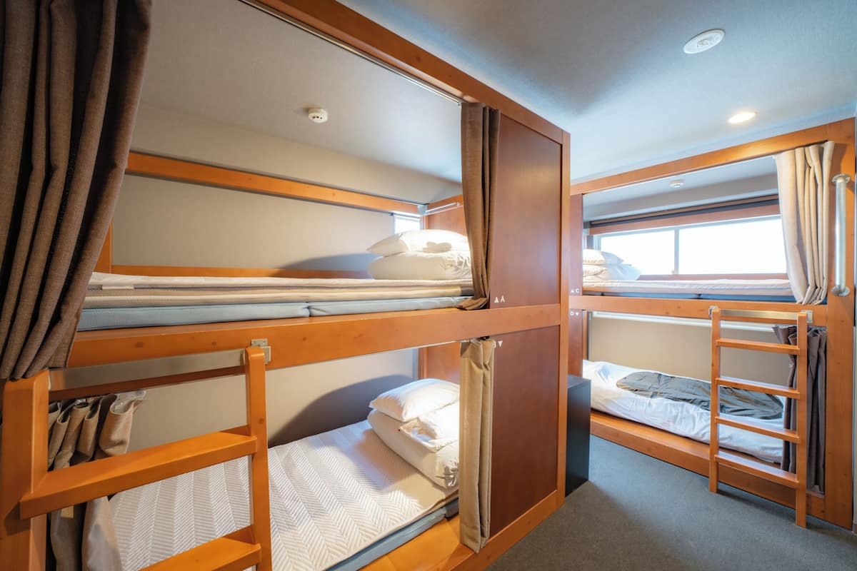 A bunk bed room with wooden frames, a window with curtains, and a ceiling light.
