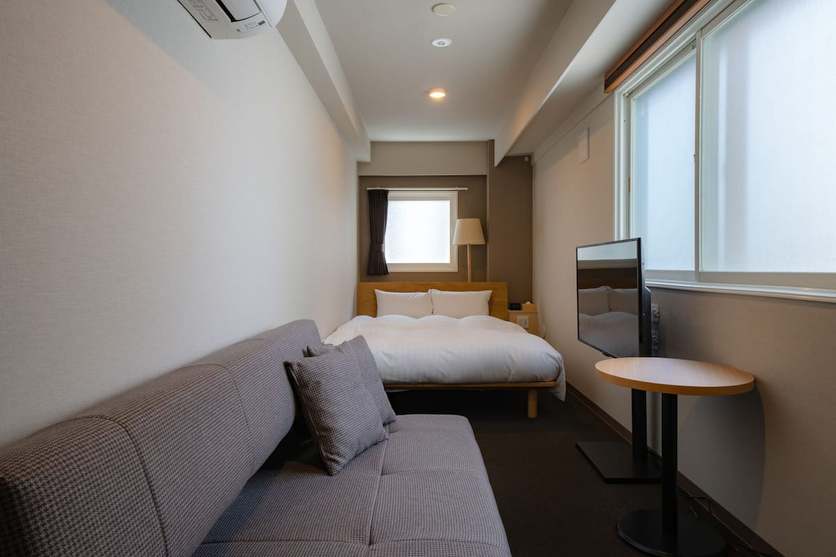 A hotel room with a bed, a sofa, a small table, a TV, and a window with curtains.
