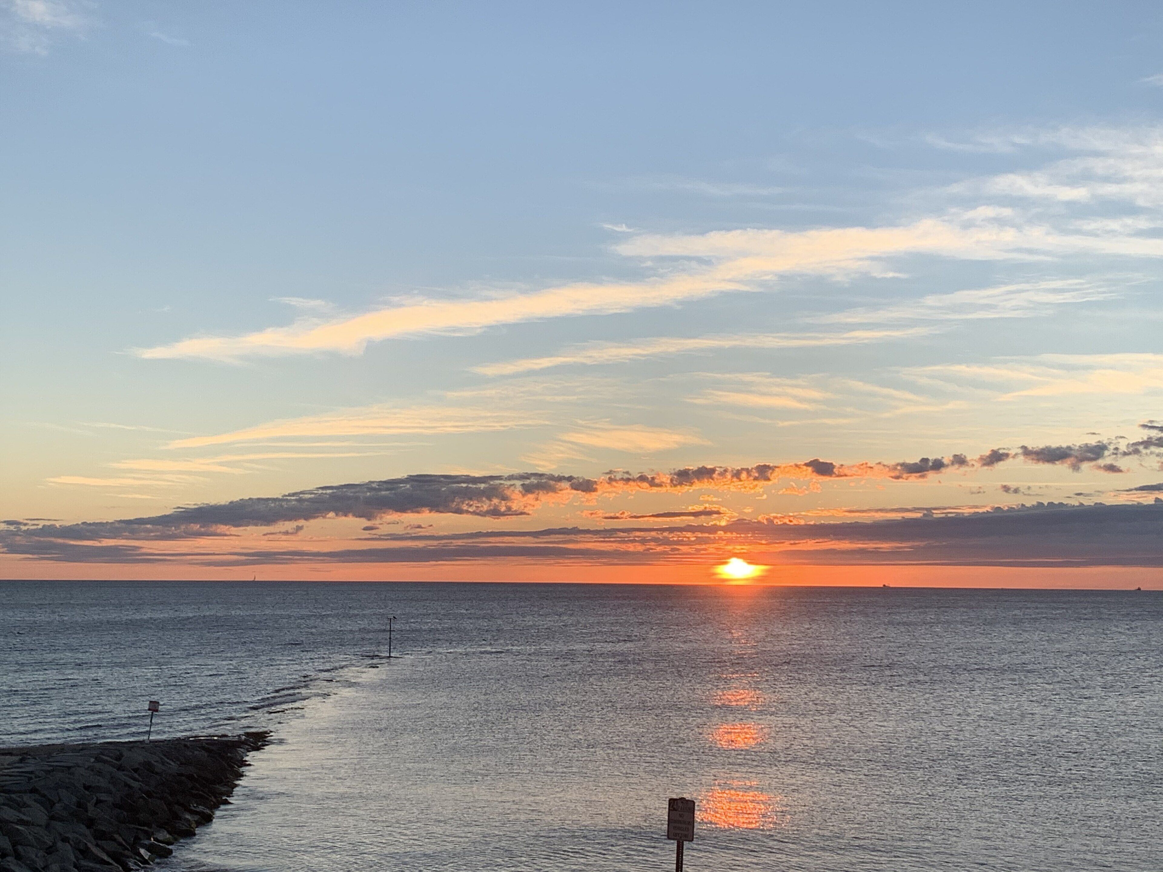 A sunset over a calm sea with a rocky shoreline and a signpost.