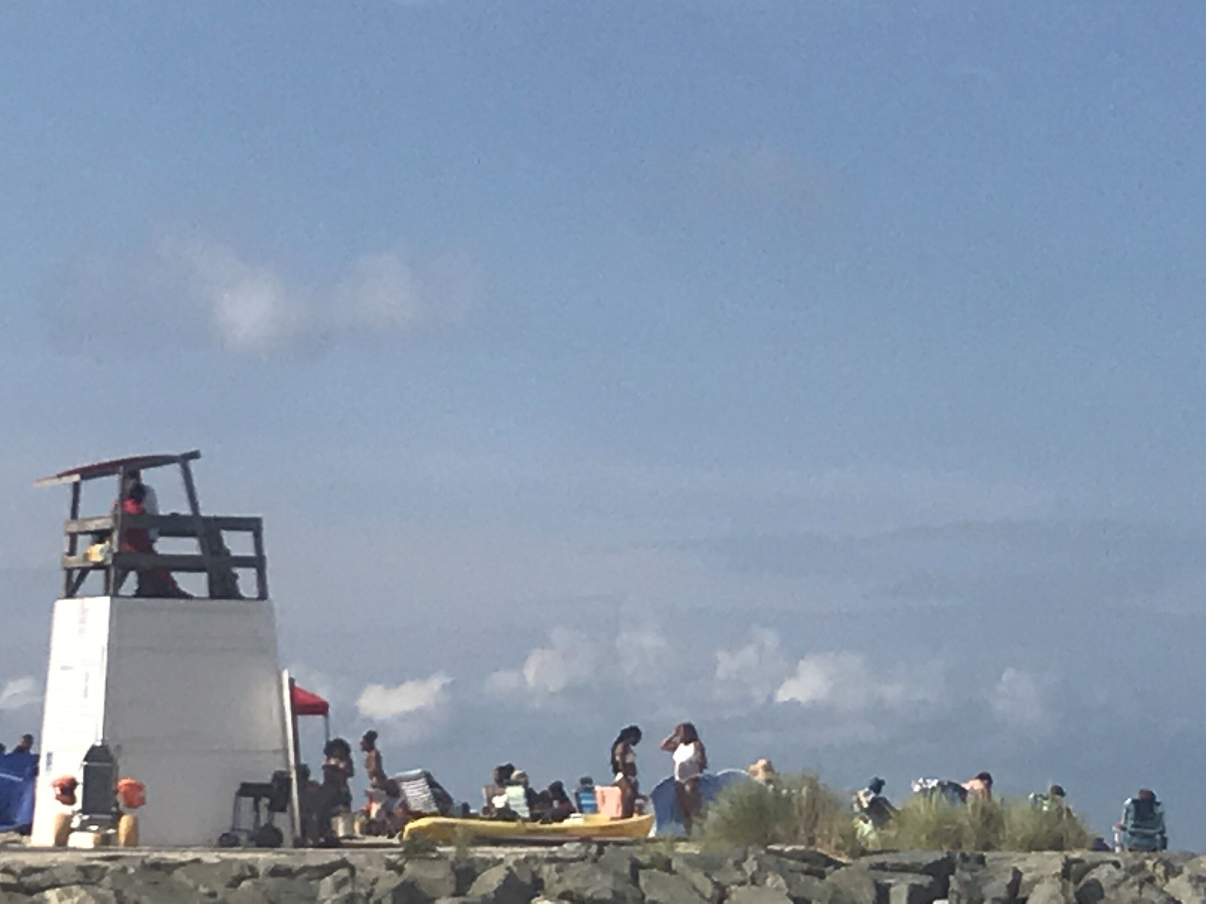 A lifeguard tower, rocky terrain, and people near the water.