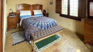 Une chambre à coucher avec un lit en bois, une table de chevet, une commode, une fenêtre donnant sur un beau paysage et un ventilateur de plafond.