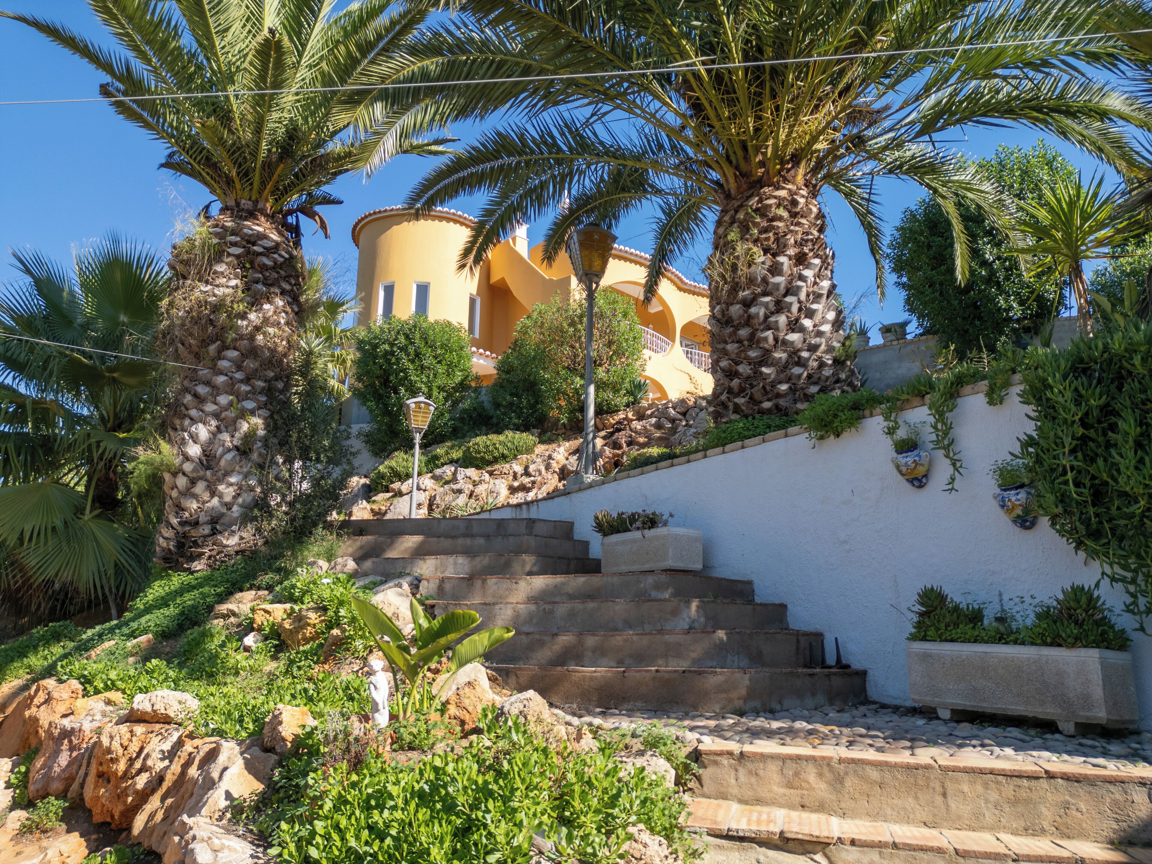 A staircase leading to a building with a yellow facade, surrounded by palm trees and greenery.