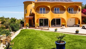 Una casa de dos pisos con fachada amarilla, varios balcones y un césped bien cuidado.