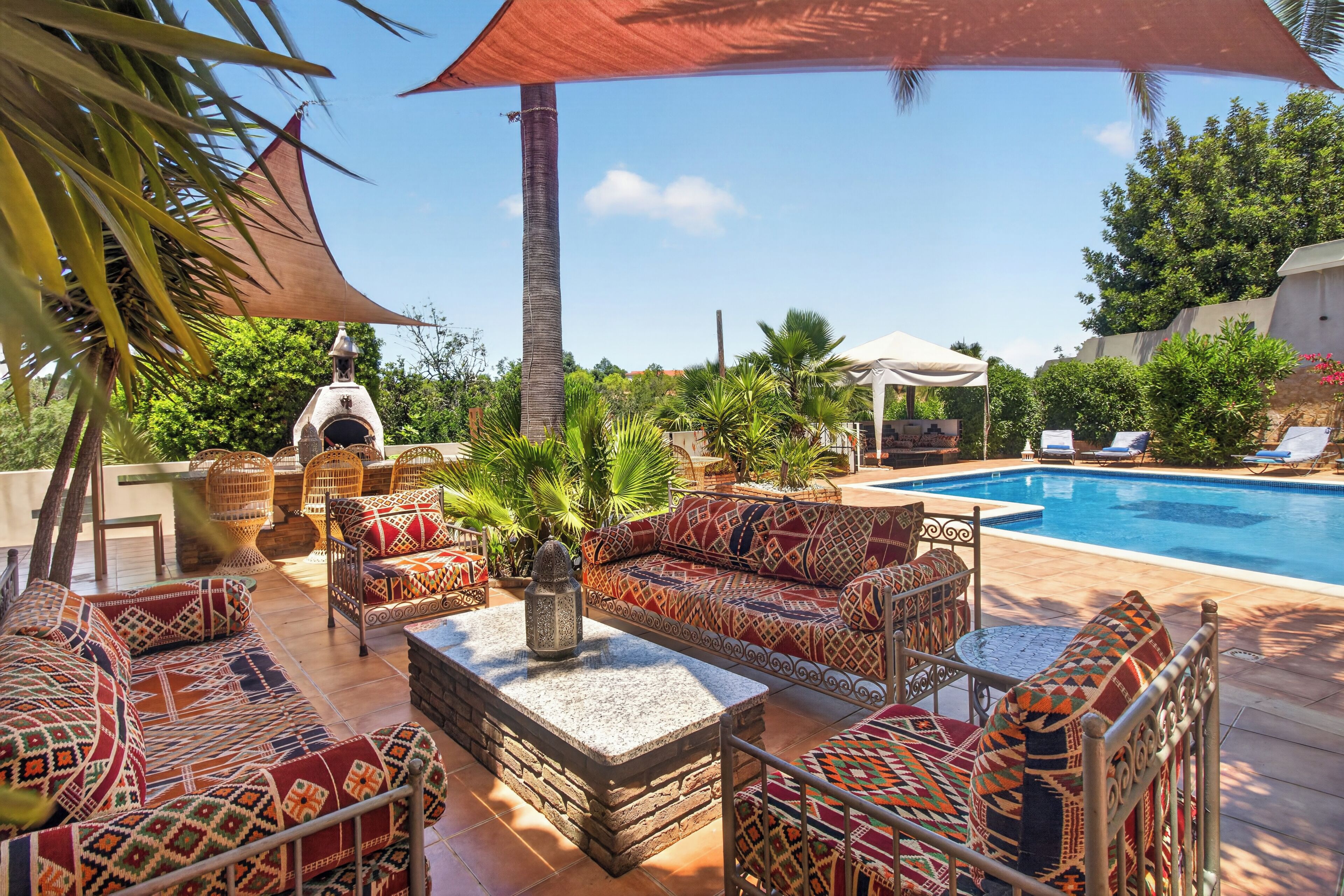 An outdoor pool area with a sofa set, a stone table, and a barbecue grill.