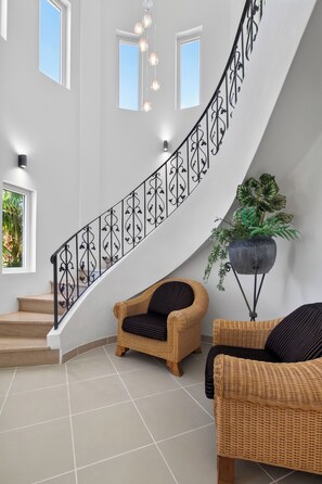 A curved staircase with a wrought iron railing, a wicker sofa, and a potted plant in a modern interior. - Two Private Pools & Waterfall in a Stunning Portuguese Villa (Armação de Pêra)