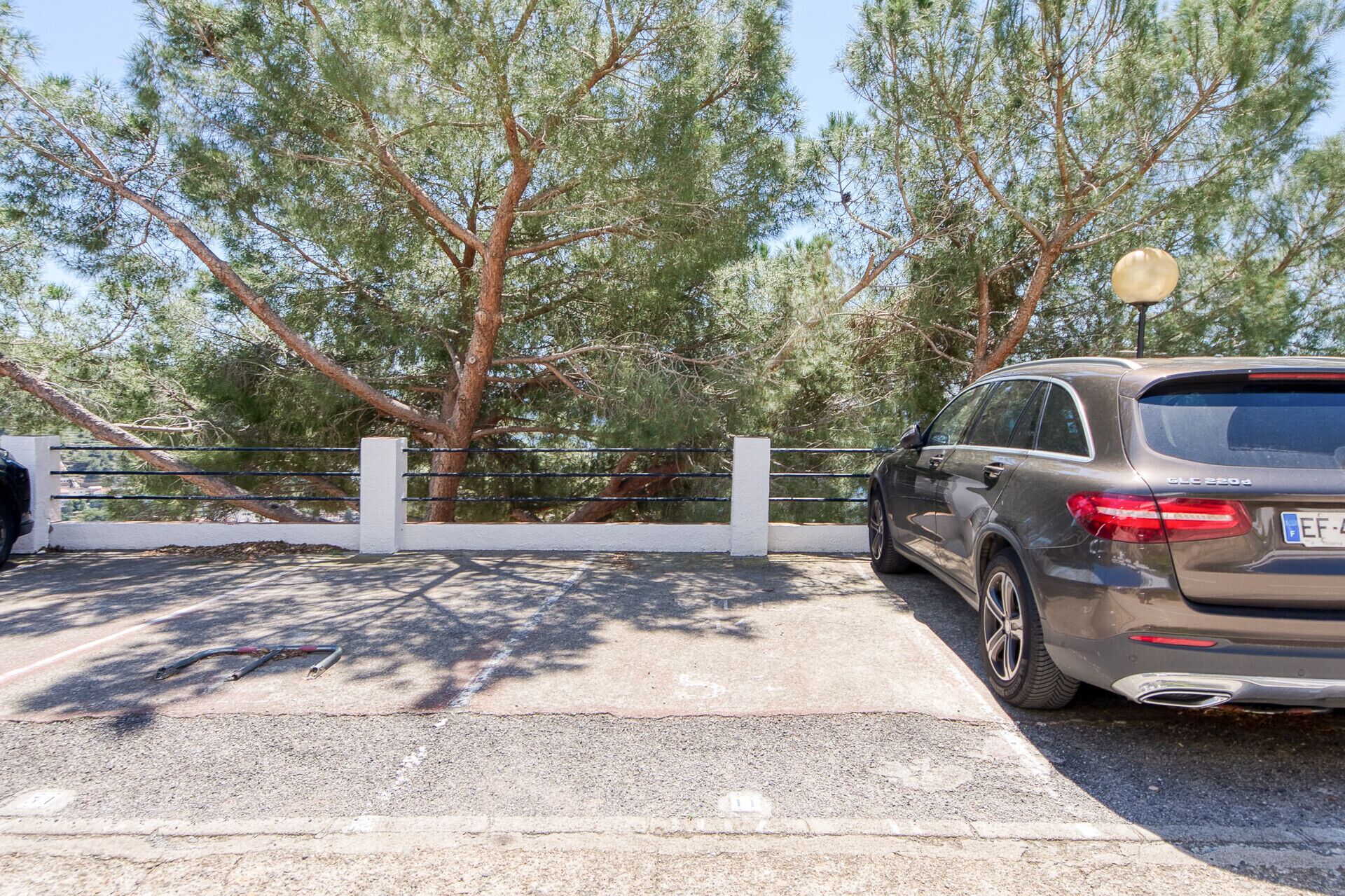 A parking area with a car, trees, and a white fence.